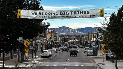 Main Street in Downtown Littleton with cars, snow-capped mountains, and a banner reading 