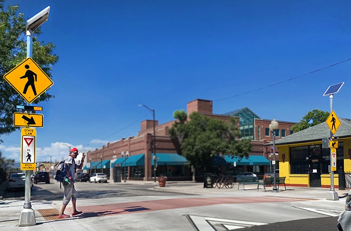 Man using raised pedestrian crosswalk and flashing beacons on Main Street.